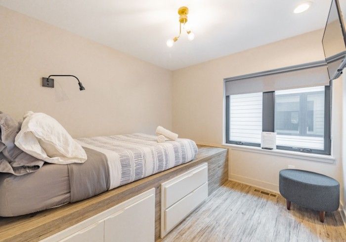 Bedroom with bed on platform with storage drawers, window, and a small chair.