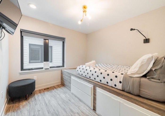 A modern bedroom featuring a bed on a raised platform with white storage drawers, a polka dot duvet, and a small bench.
