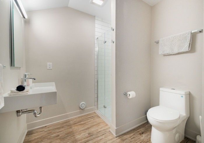 Modern bathroom with floating sink, glass shower, and toilet on wood-look tile floor