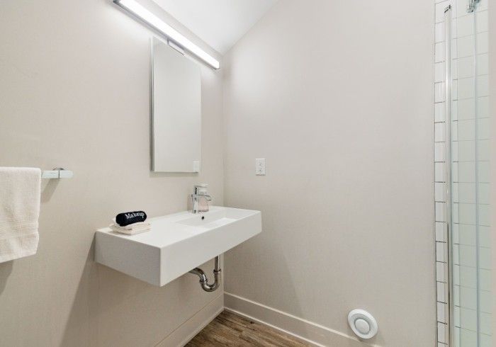 Bathroom with floating white sink, mirror, shower, and towel bar. Light walls and wood-look floor.