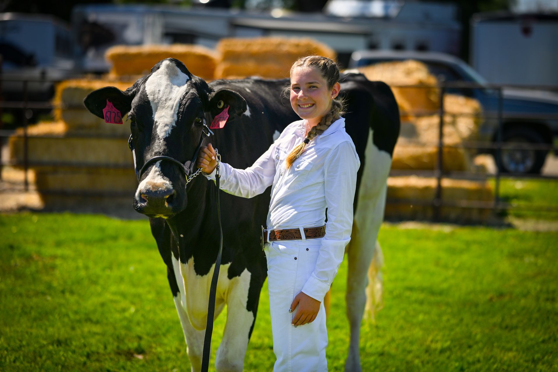 Young person in white attire smiling next to a black and white cow in a grassy area.