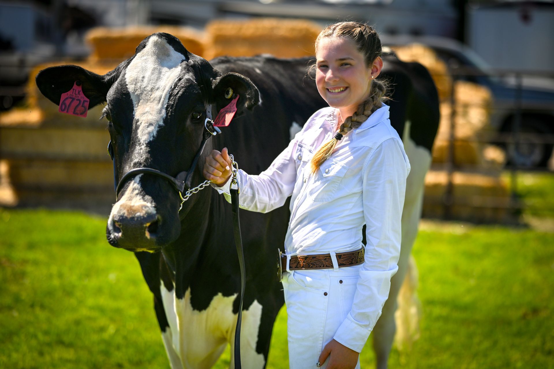 Girl in white outfit stands next to a black and white cow in a field.
