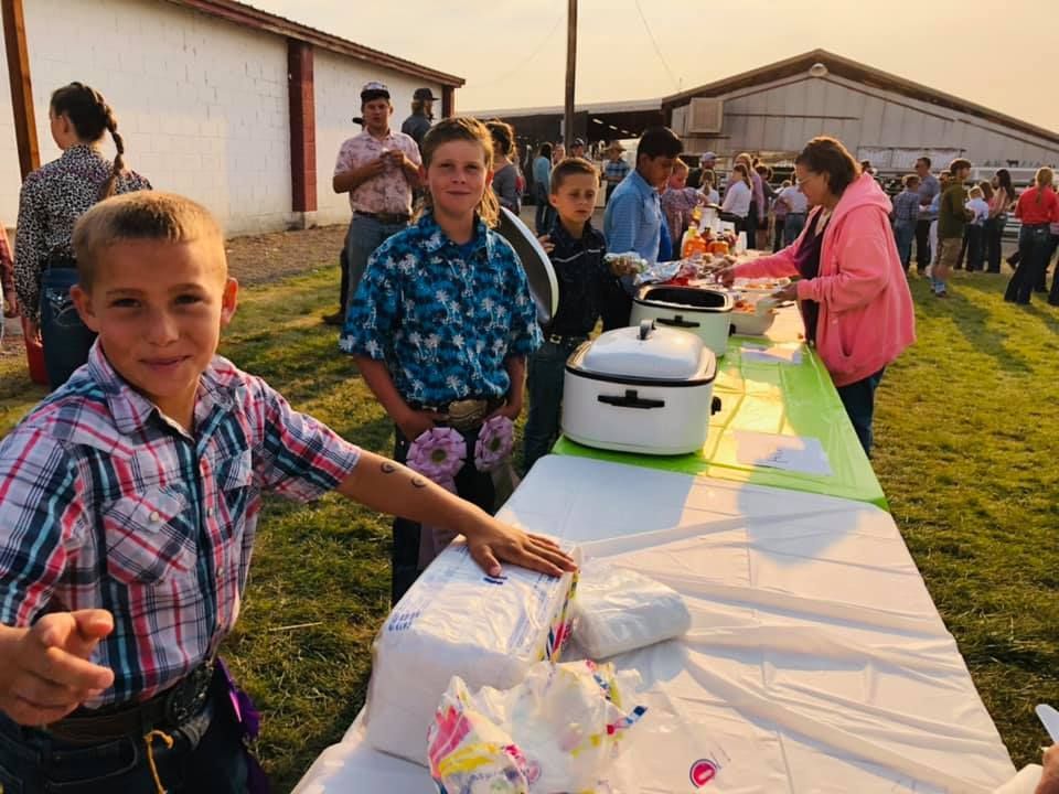 A boy is pointing at the camera while standing in front of a long table.