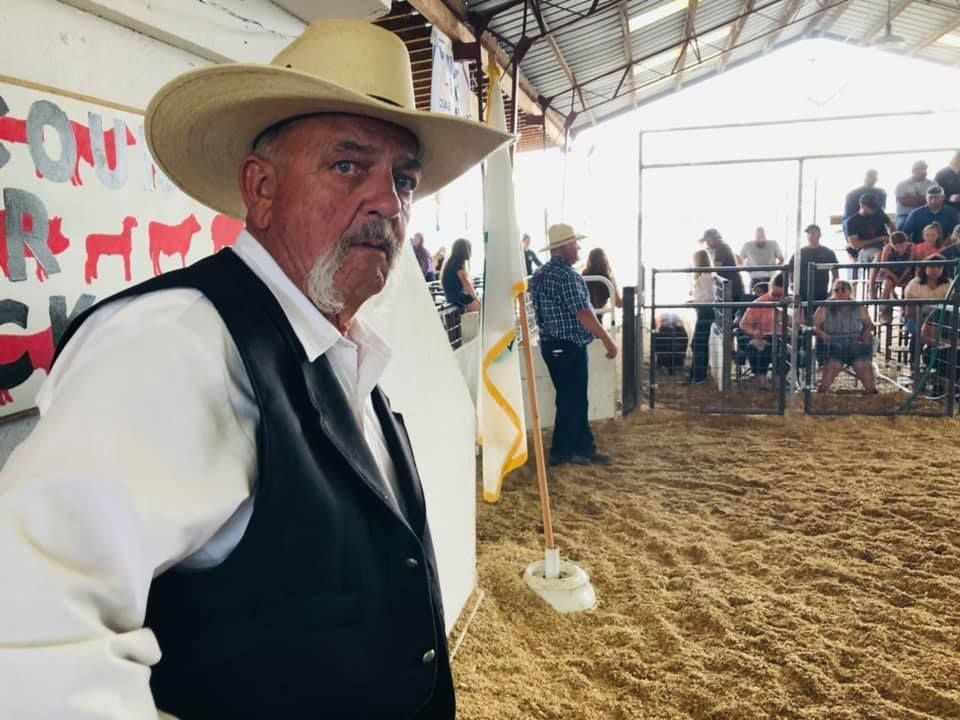 A man wearing a cowboy hat and vest is standing in a barn.
