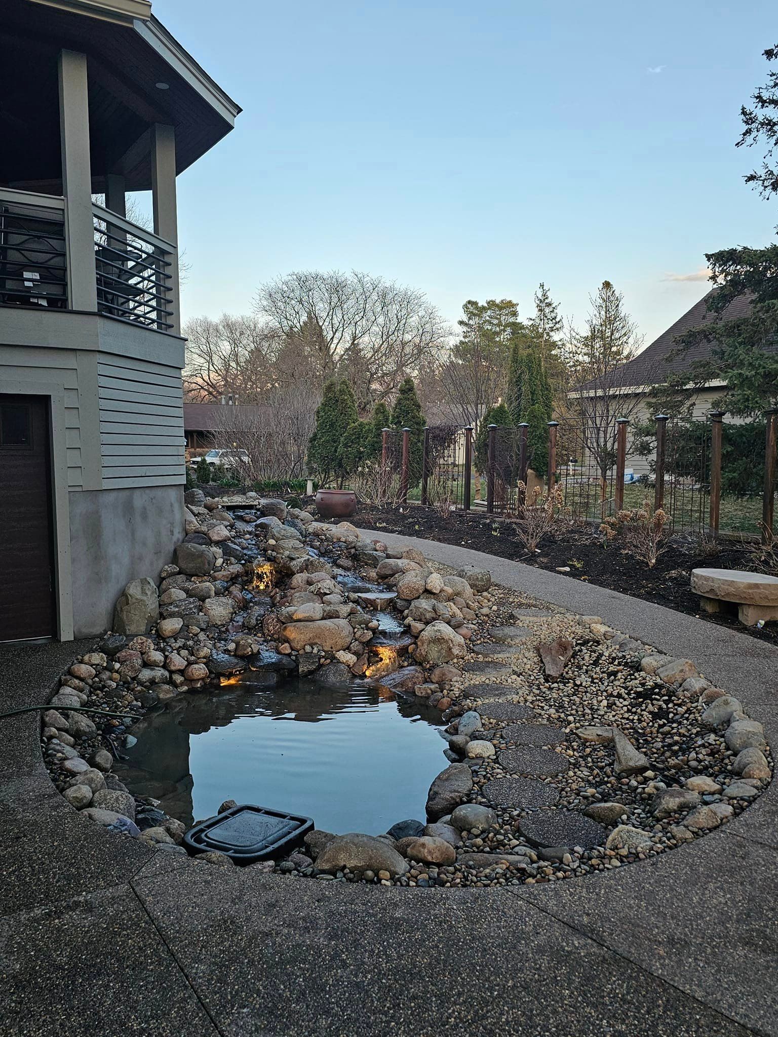 A small pond surrounded by rocks in front of a house.