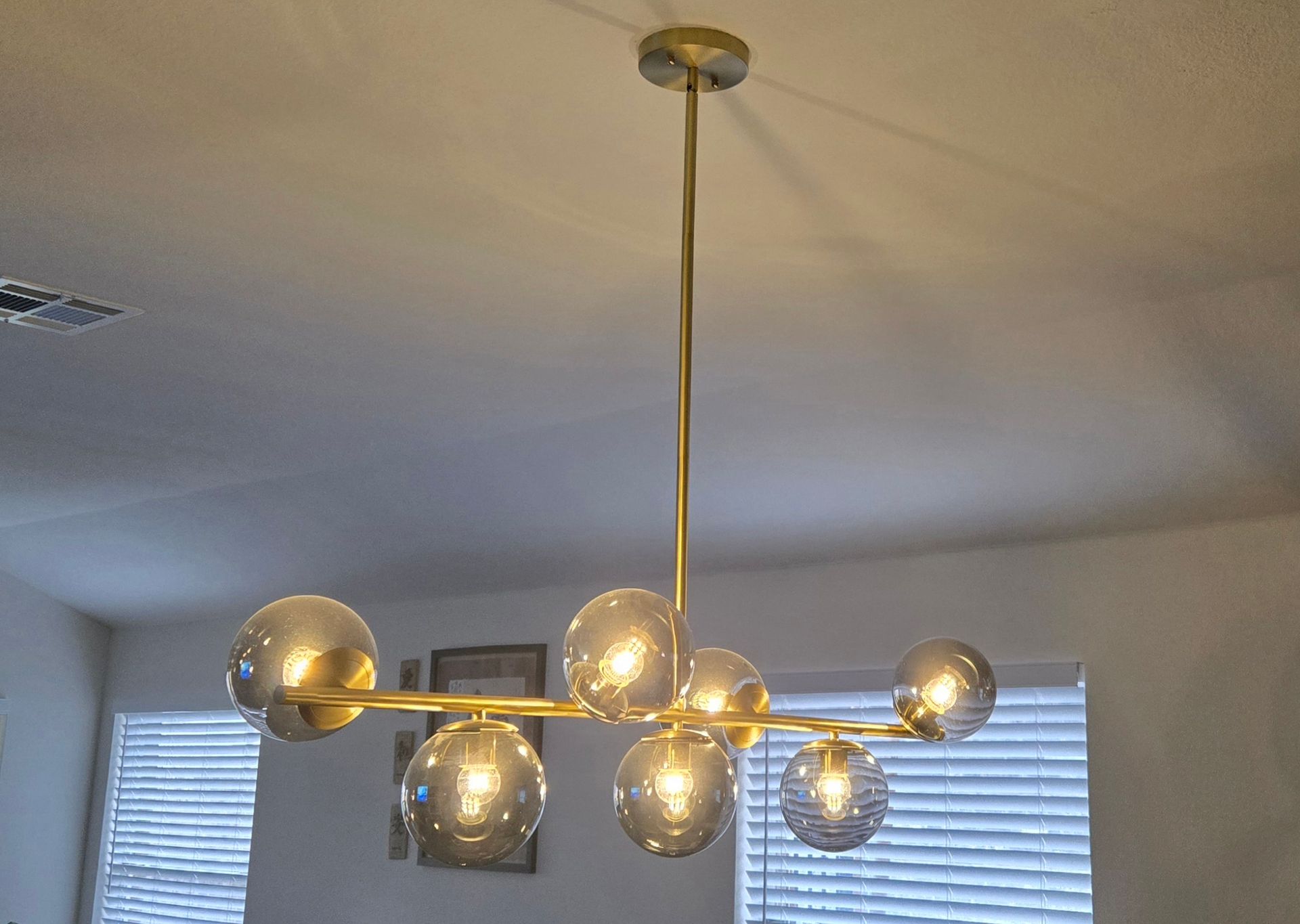 Modern gold chandelier with globe bulbs hanging from a ceiling near a window with blinds