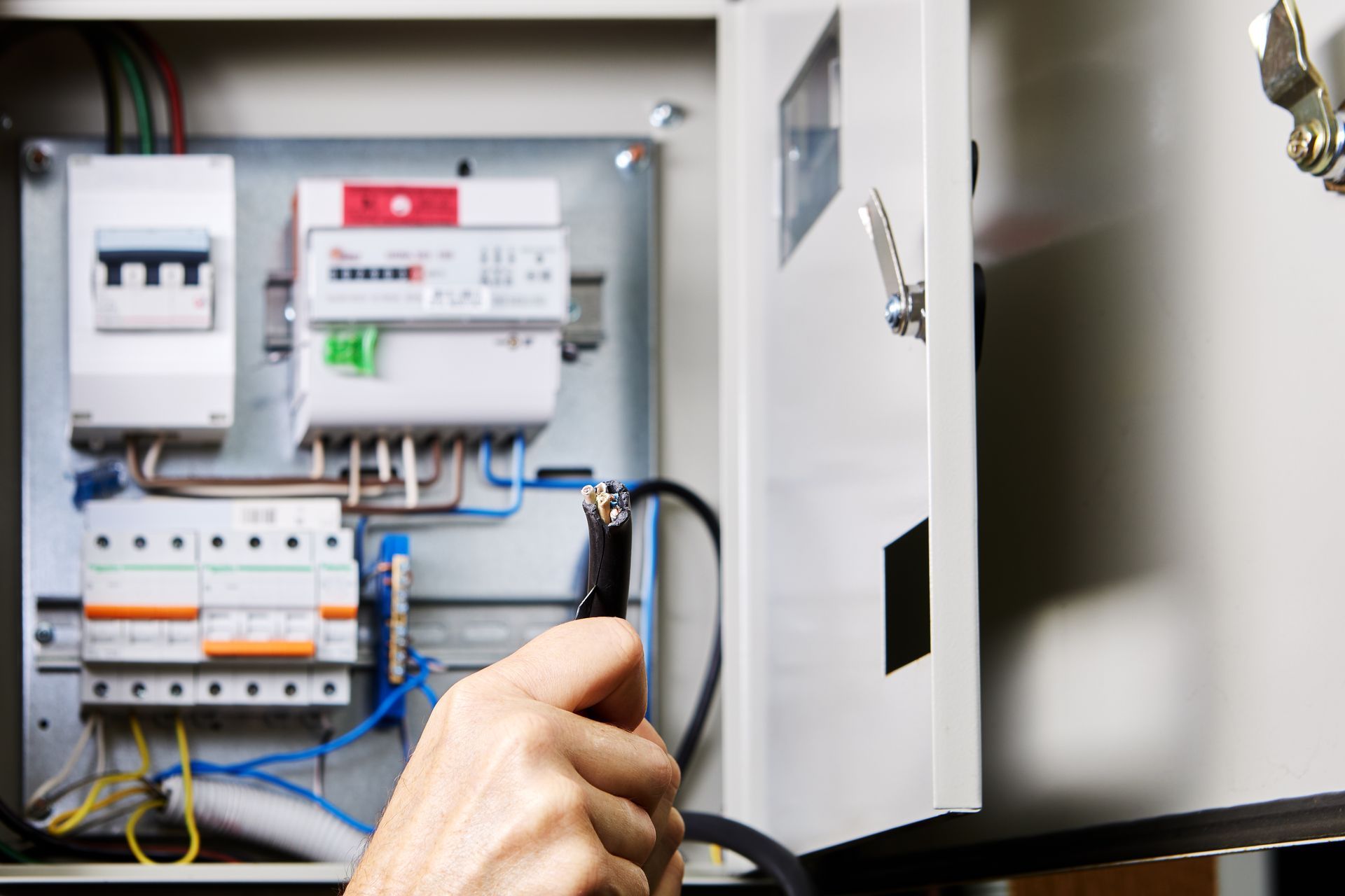 Hand holding a cable inside an open electrical control panel with circuit breakers and wiring