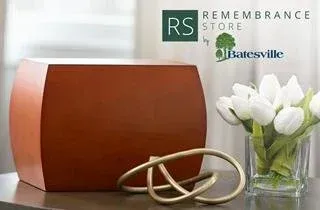 Orange cremation urn with metal cremation jewelry and white tulips beside a remembrance store logo