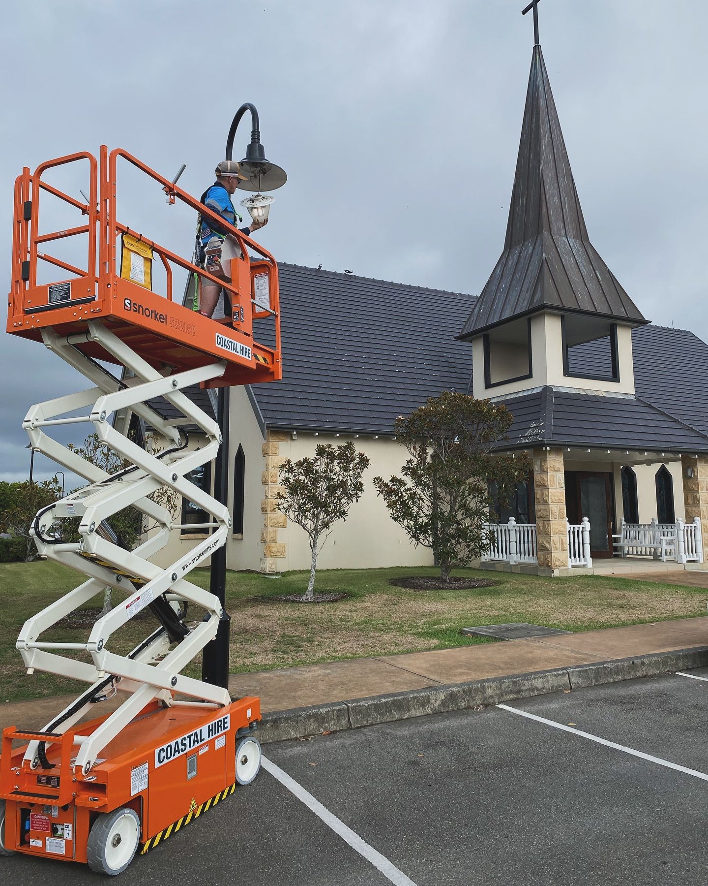 A Man is Standing on a Scissor Lift in Front of a Church — J T Walker Solar & Electrical In Gloucester, NSW