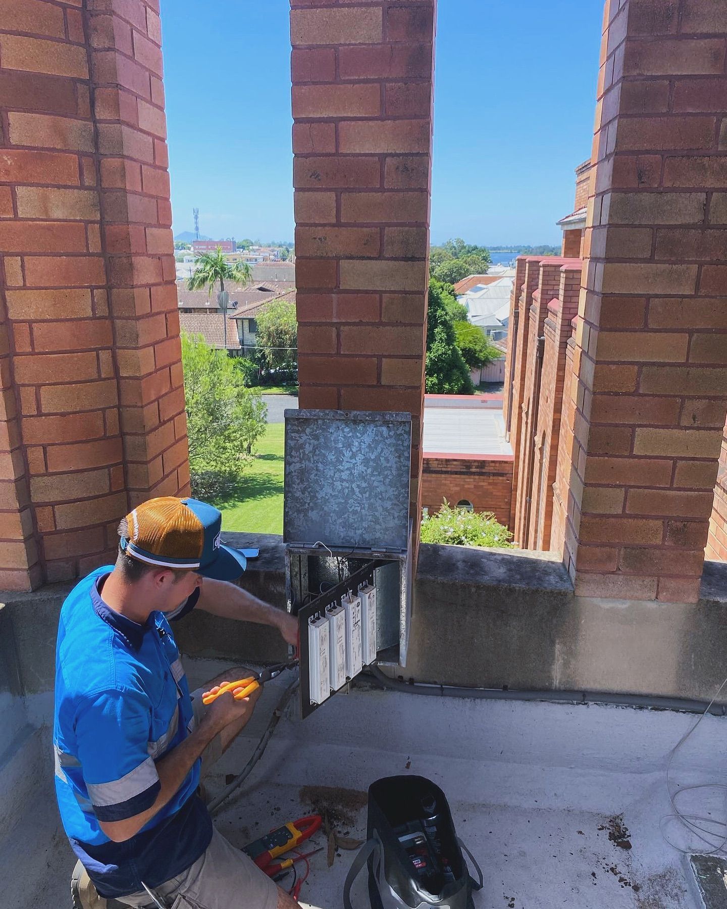 A Man is Sitting on a Balcony Working on a Chimney — J T Walker Solar & Electrical In Taree, NSW