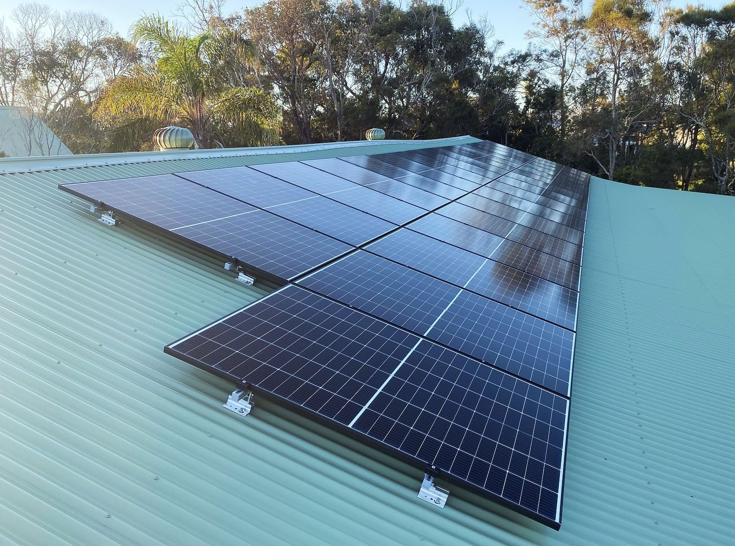 Solar Panels Installed On A Green, Corrugated Metal Roof, Reflecting Sunlight — J T Walker Solar & Electrical In Taree, NSW