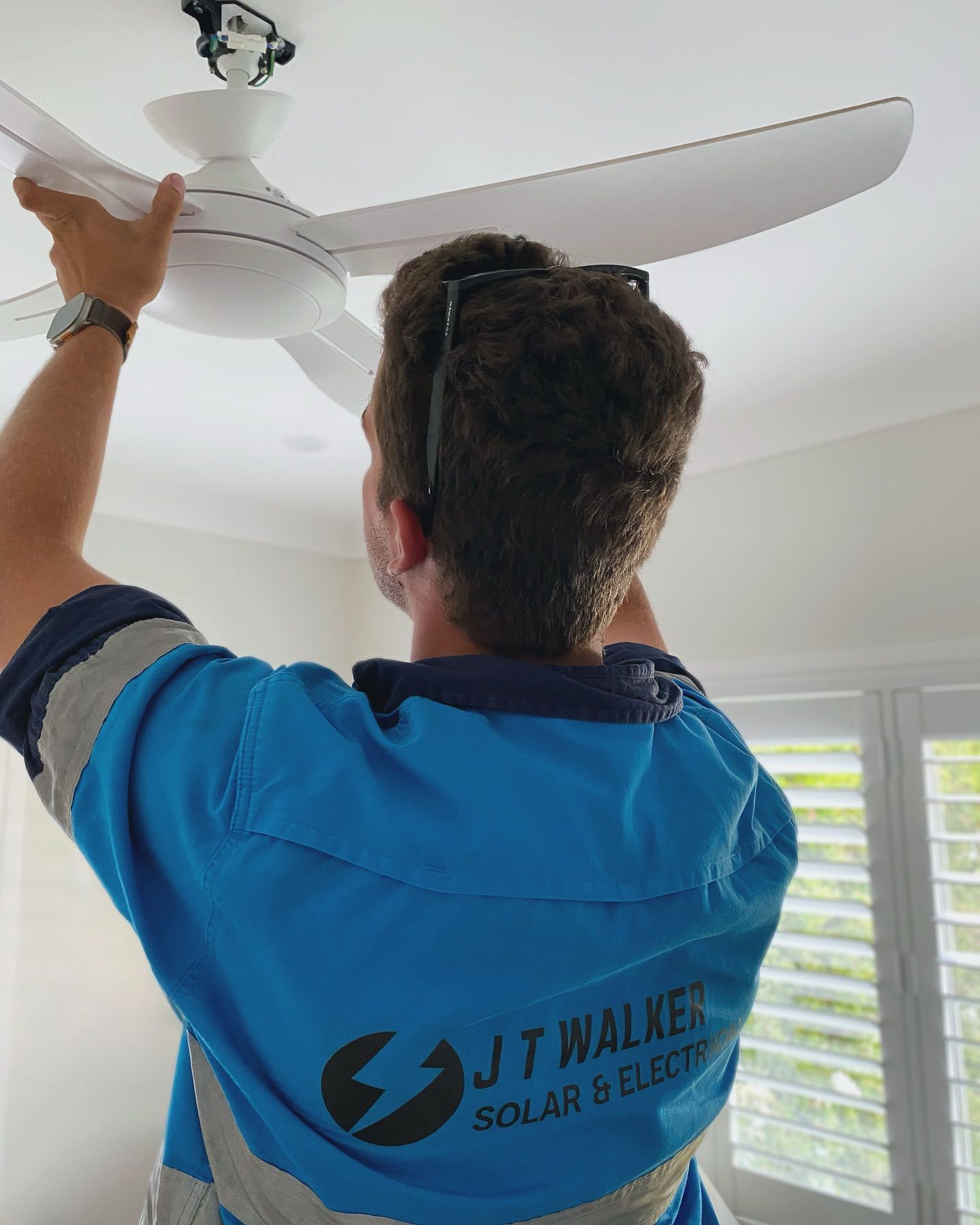 Man In Blue Shirt Installs Ceiling Fan; Interior Setting — J T Walker Solar & Electrical In Taree, NSW