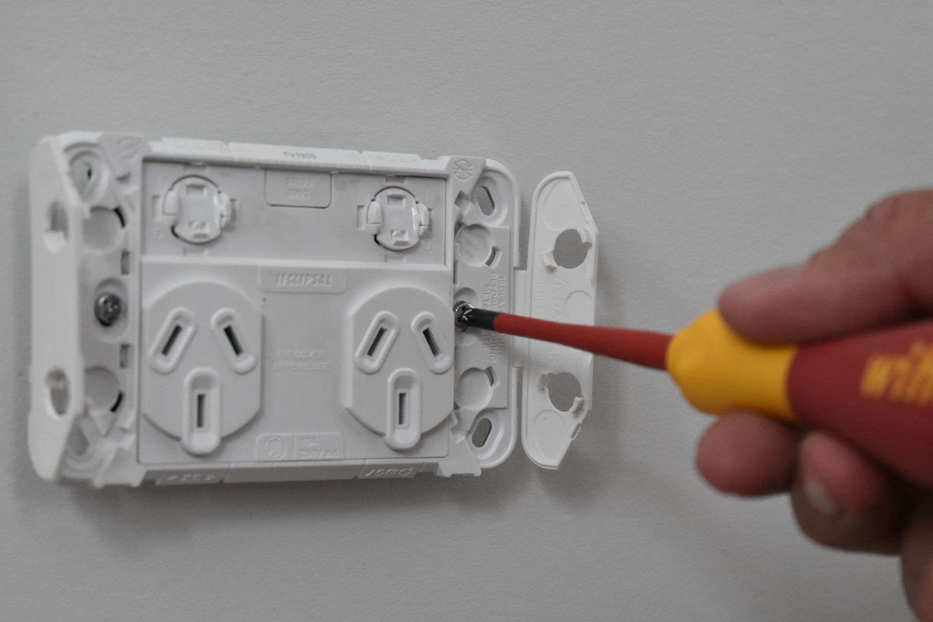 A Person Uses A Screwdriver To Secure A White Electrical Outlet To A Wall — J T Walker Solar & Electrical In Wingham, NSW
