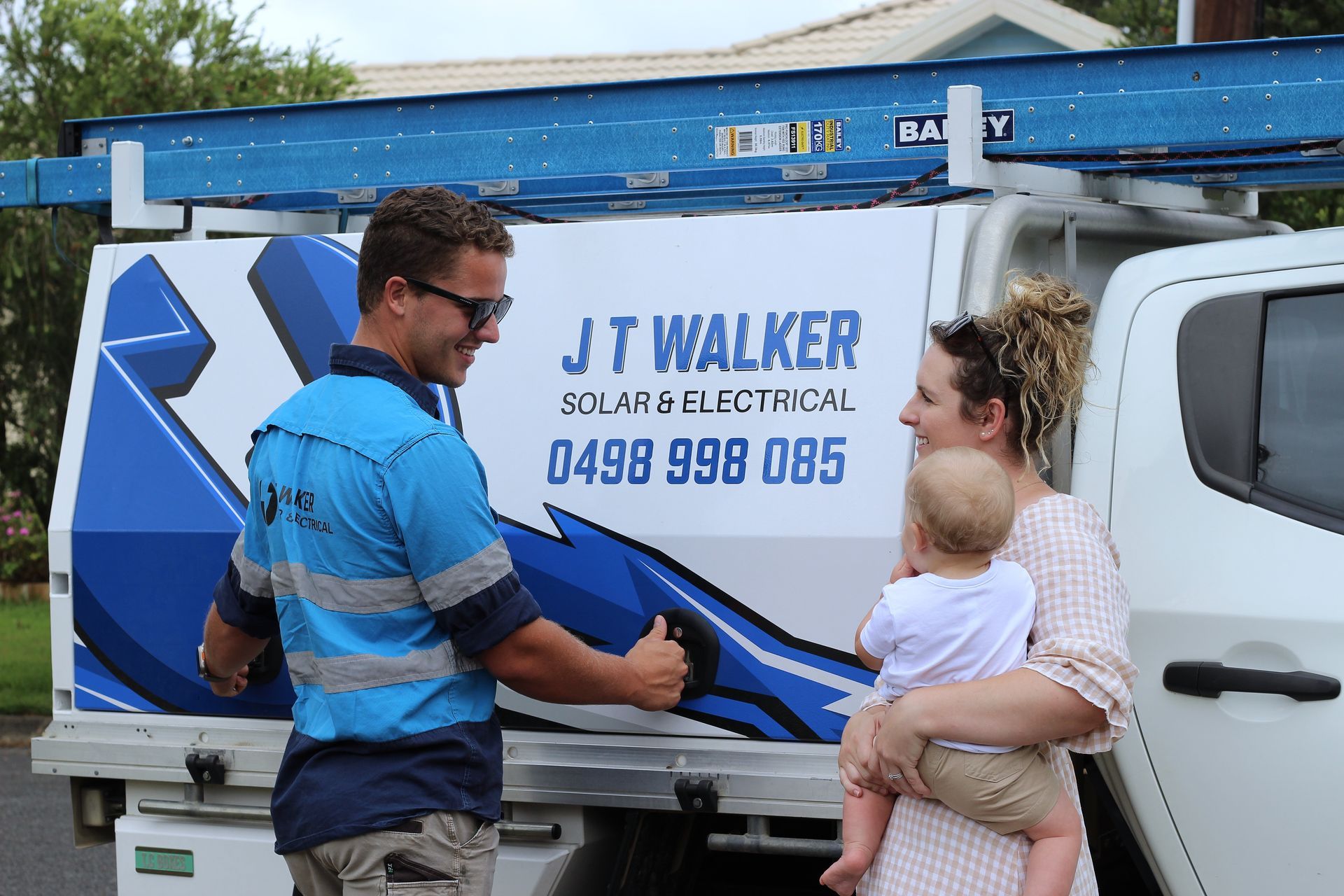 A Solar And Electrical Technician Talking To A Woman Holding A Baby Next To A Work Truck — J T Walker Solar & Electrical In Taree, NSW