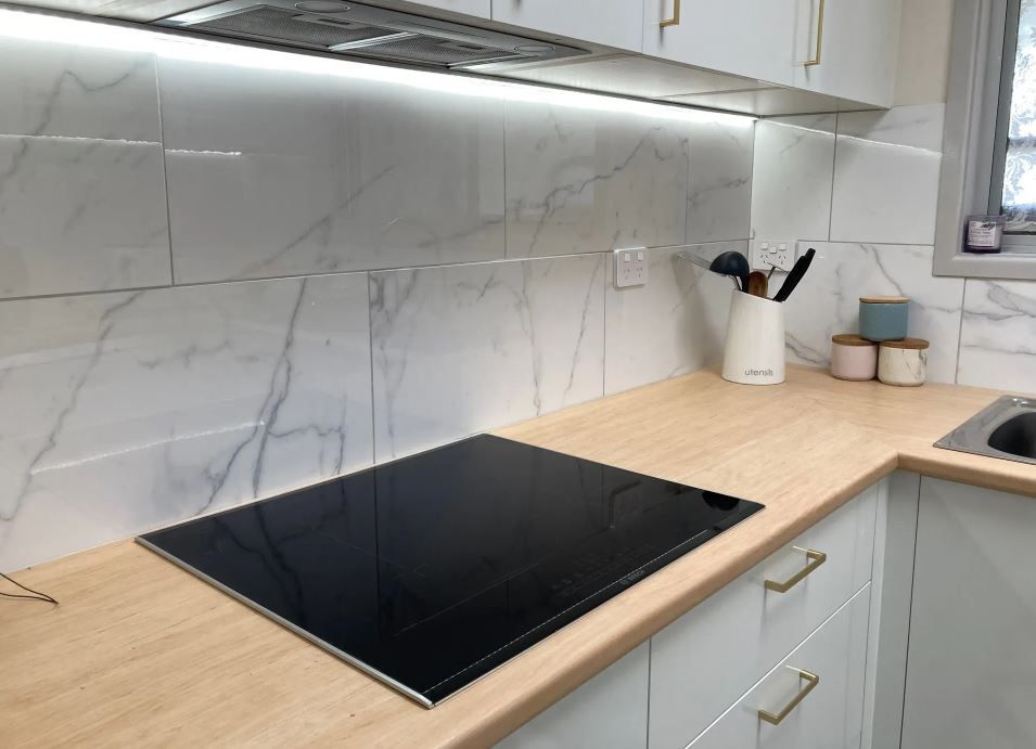 A Kitchen With White Cabinets and a Black Stove Top Oven — J T Walker Solar & Electrical In Taree, NSW