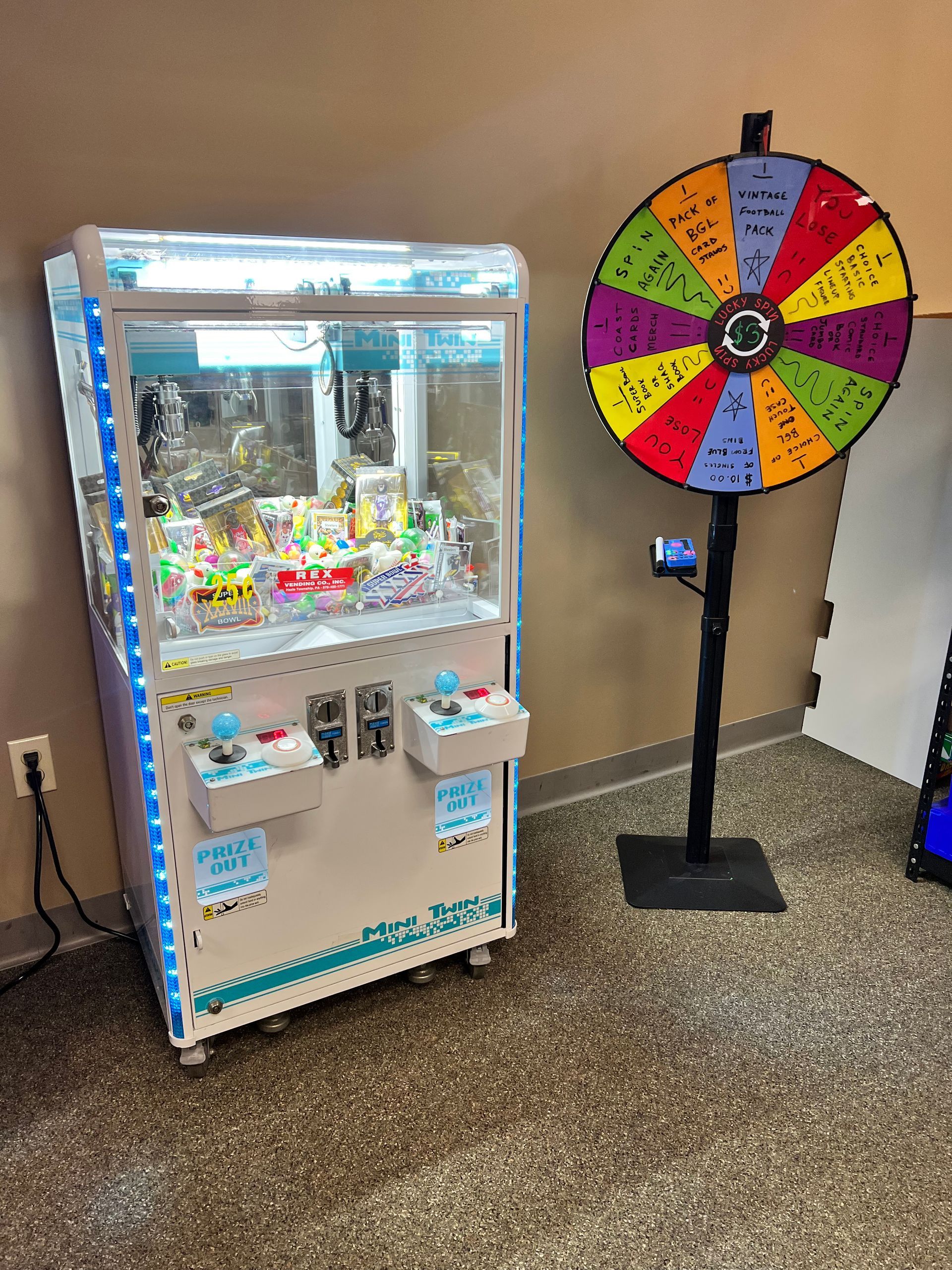 A claw machine and a wheel of fortune are sitting next to each other in a room.