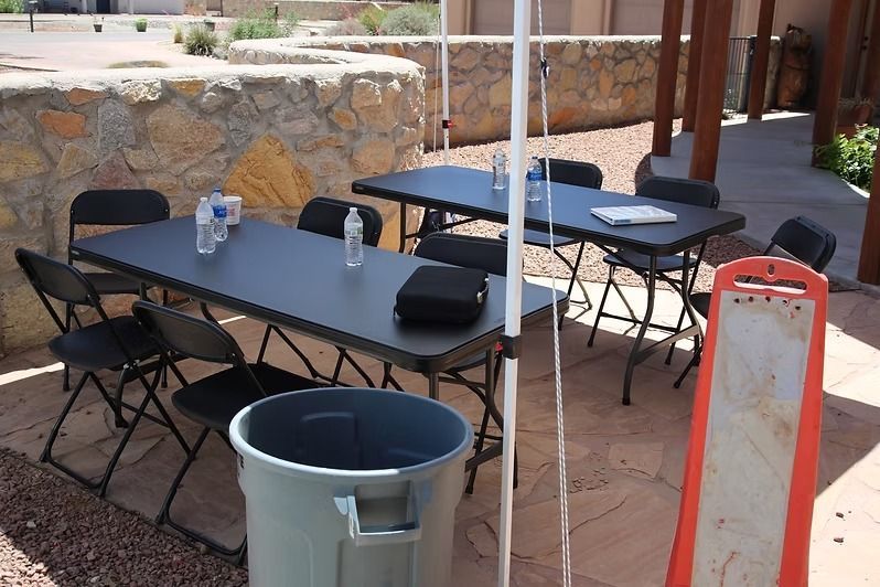 Outdoor patio with black tables and folding chairs, a gray trash can, and a stone wall in the background