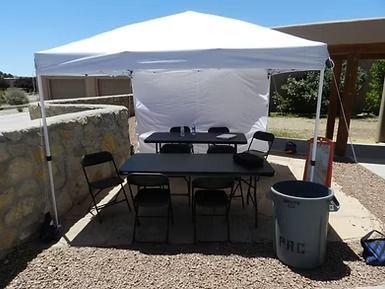 White canopy tent shading a table and chairs beside a stone wall and trash can outdoors