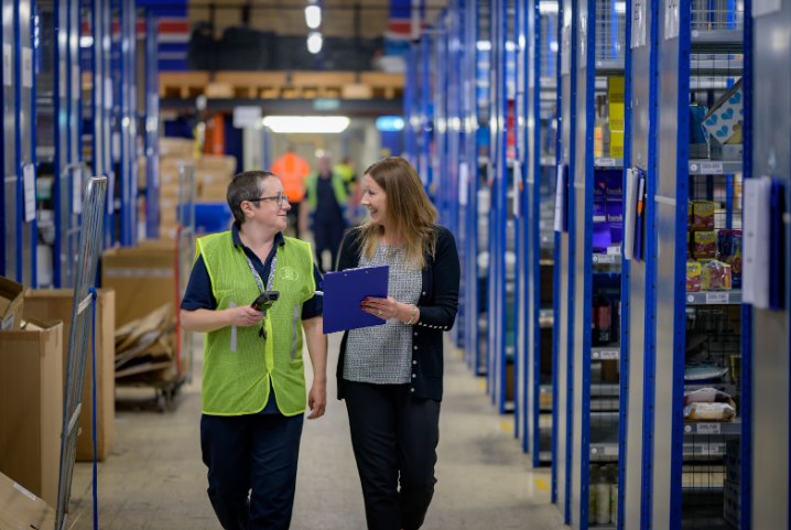 Two women are walking through a warehouse talking to each other.