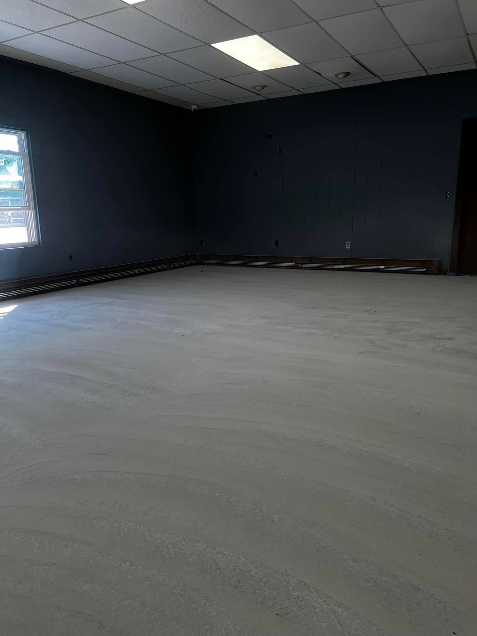 Empty room with gray floor, dark walls, and a grid ceiling under fluorescent lighting