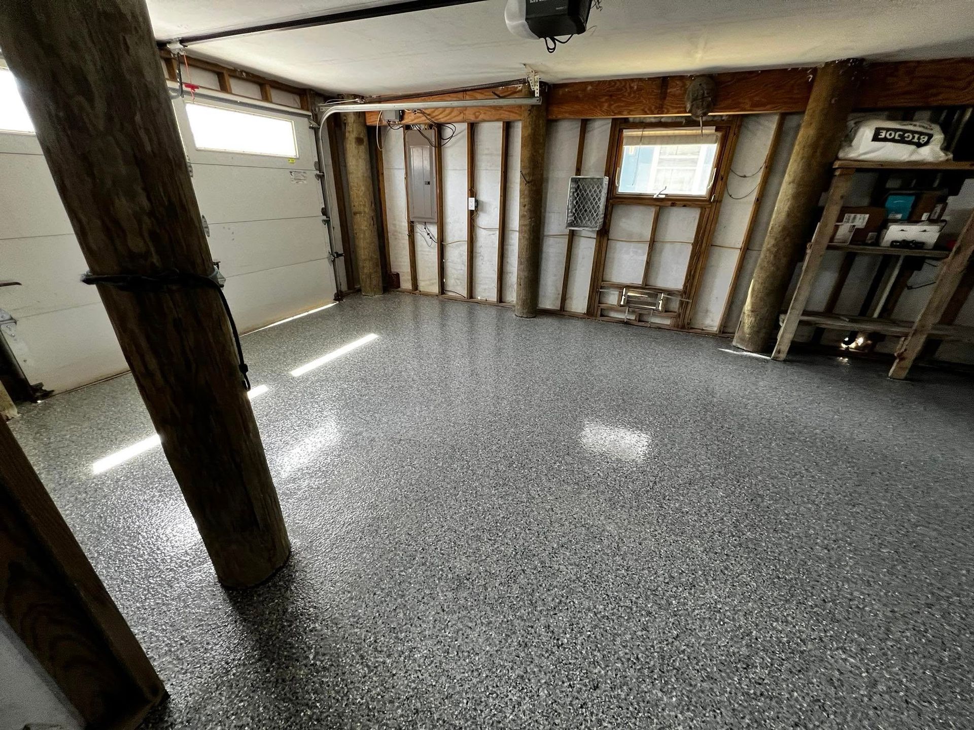 Empty unfinished basement with concrete floor, exposed studs, and garage door on the left.