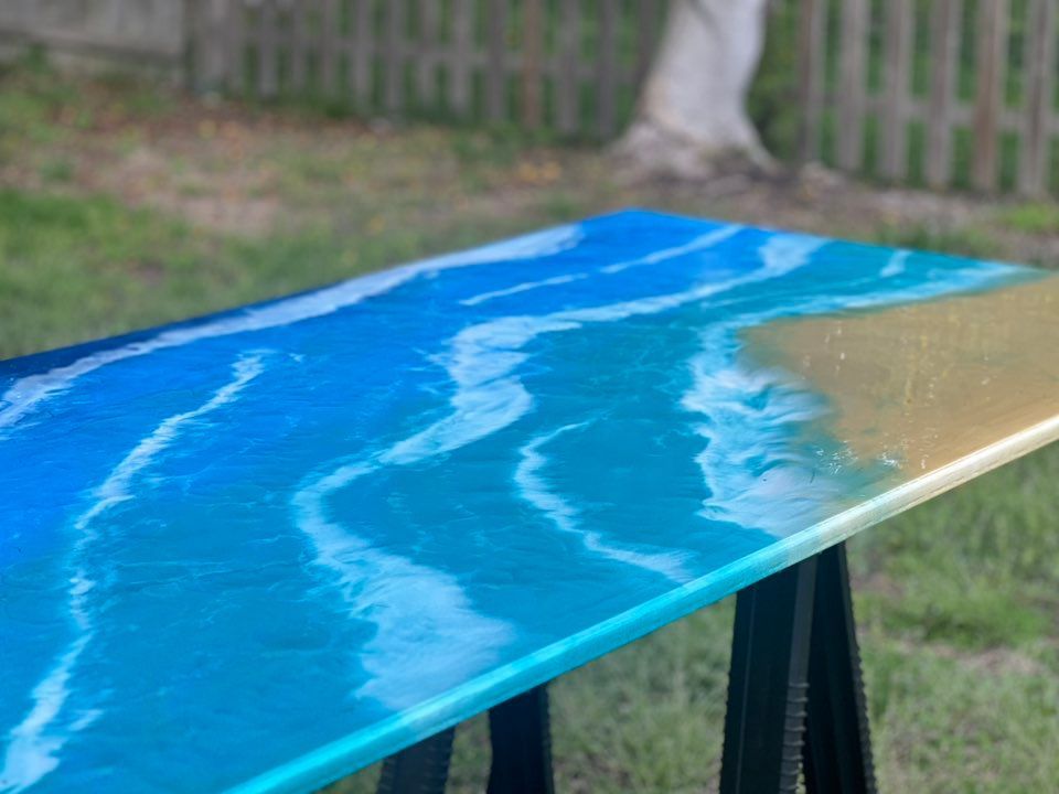 Blue resin-coated tabletop with white swirls, supported on sawhorses outdoors in a yard