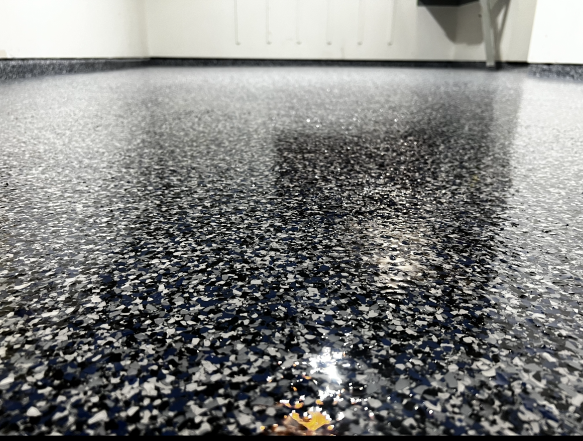 Close-up of a glossy black speckled floor with a white wall in the background