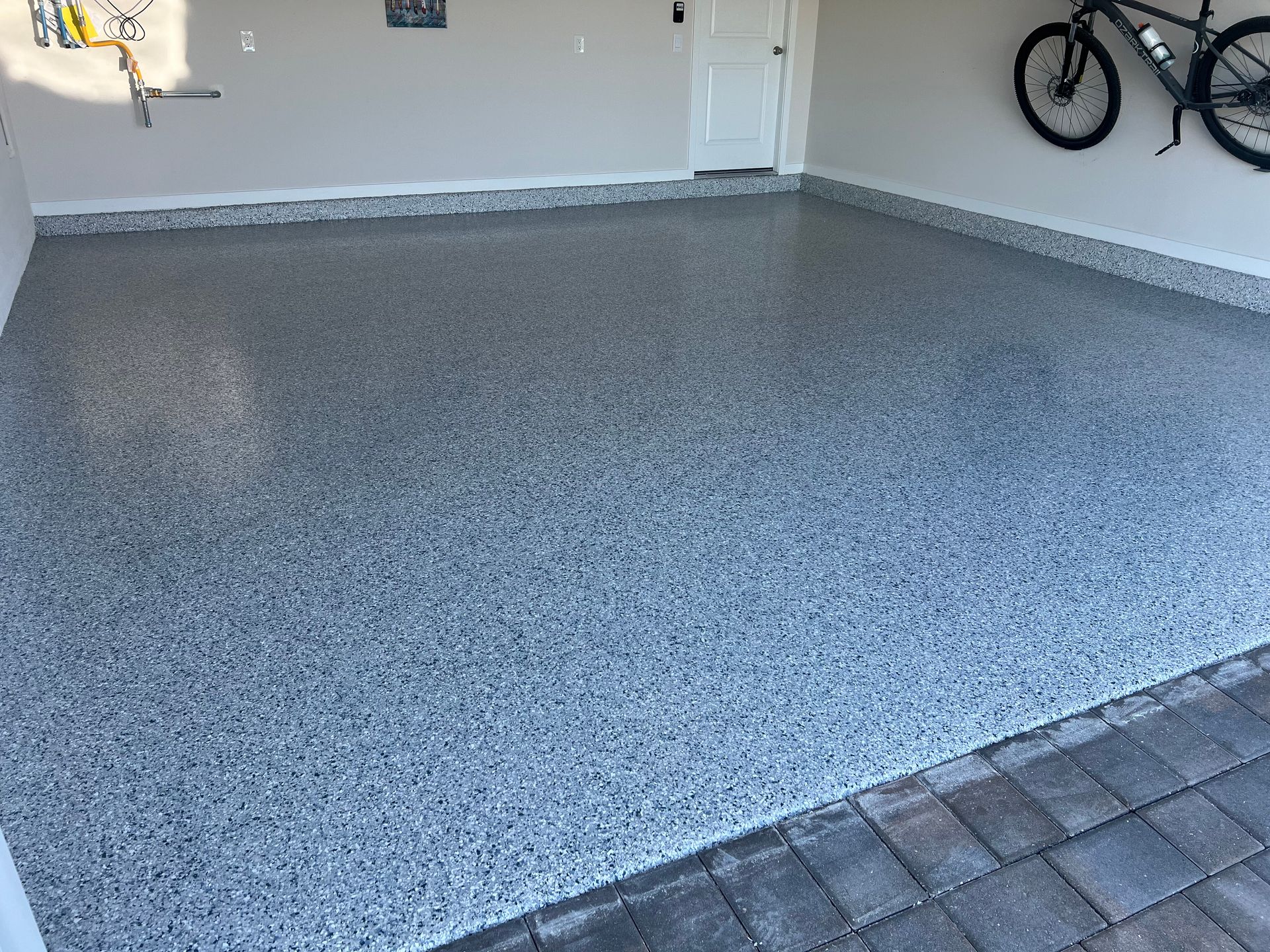 Empty speckled epoxy garage floor with bicycles mounted on the wall and a door in the background