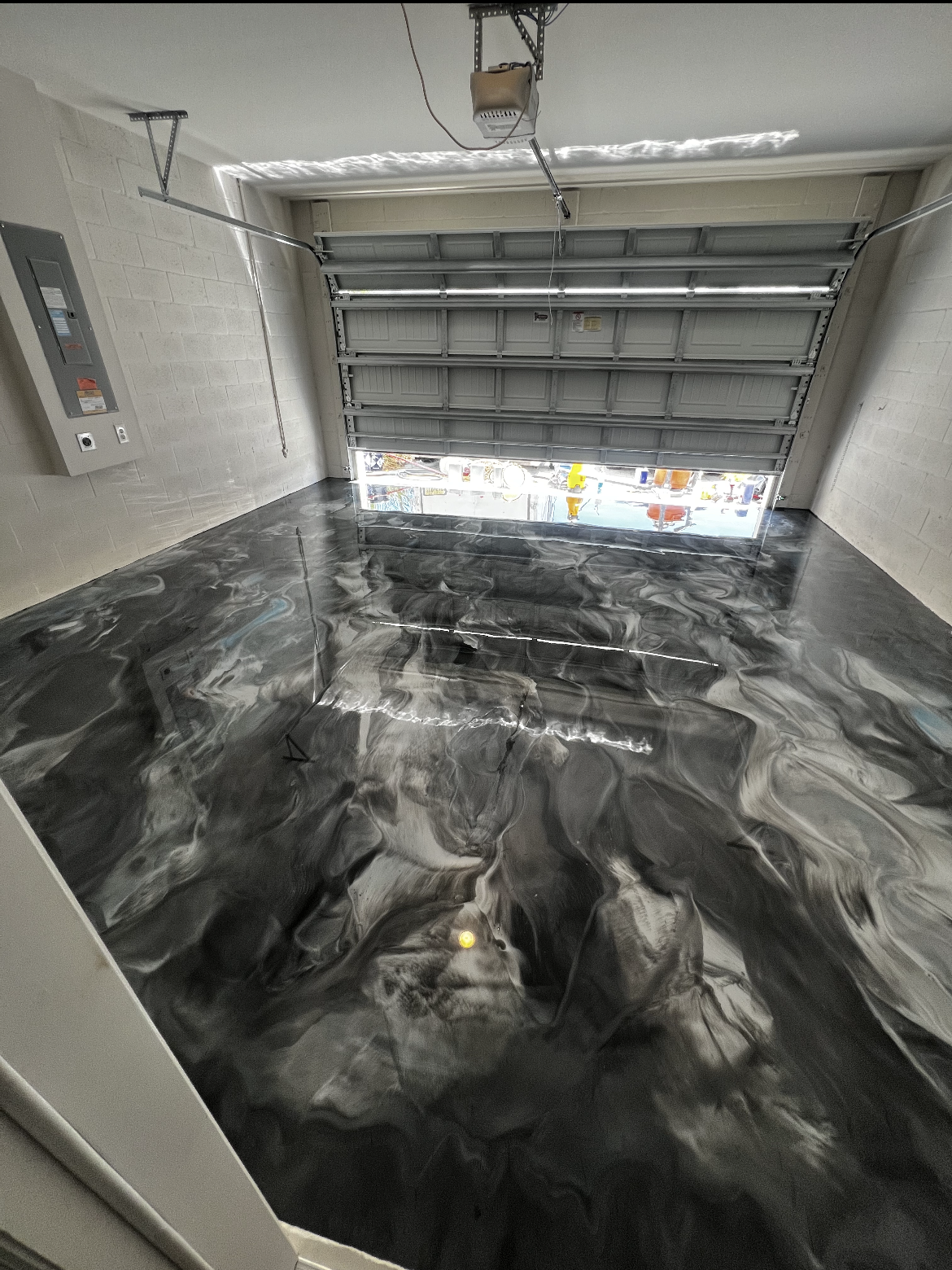 Empty garage with a glossy black-and-white marbled floor and an open garage door.