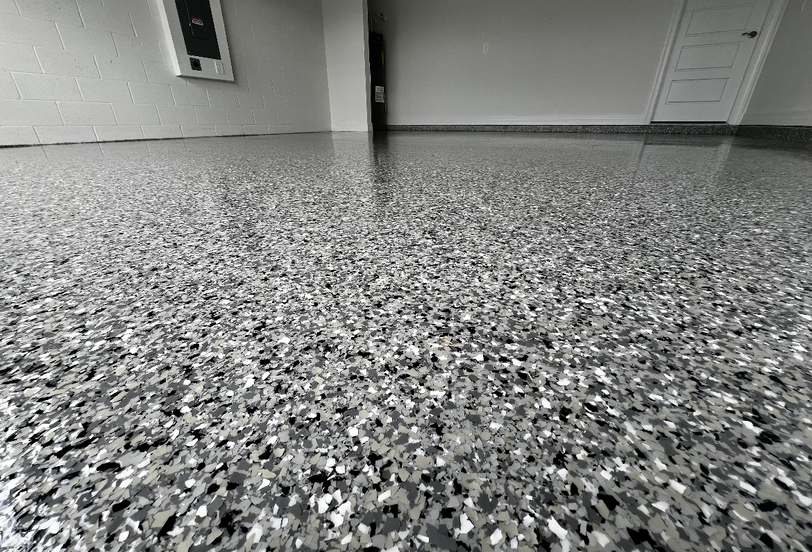 Gray speckled epoxy floor in a garage with a closed door and wall vent in the background