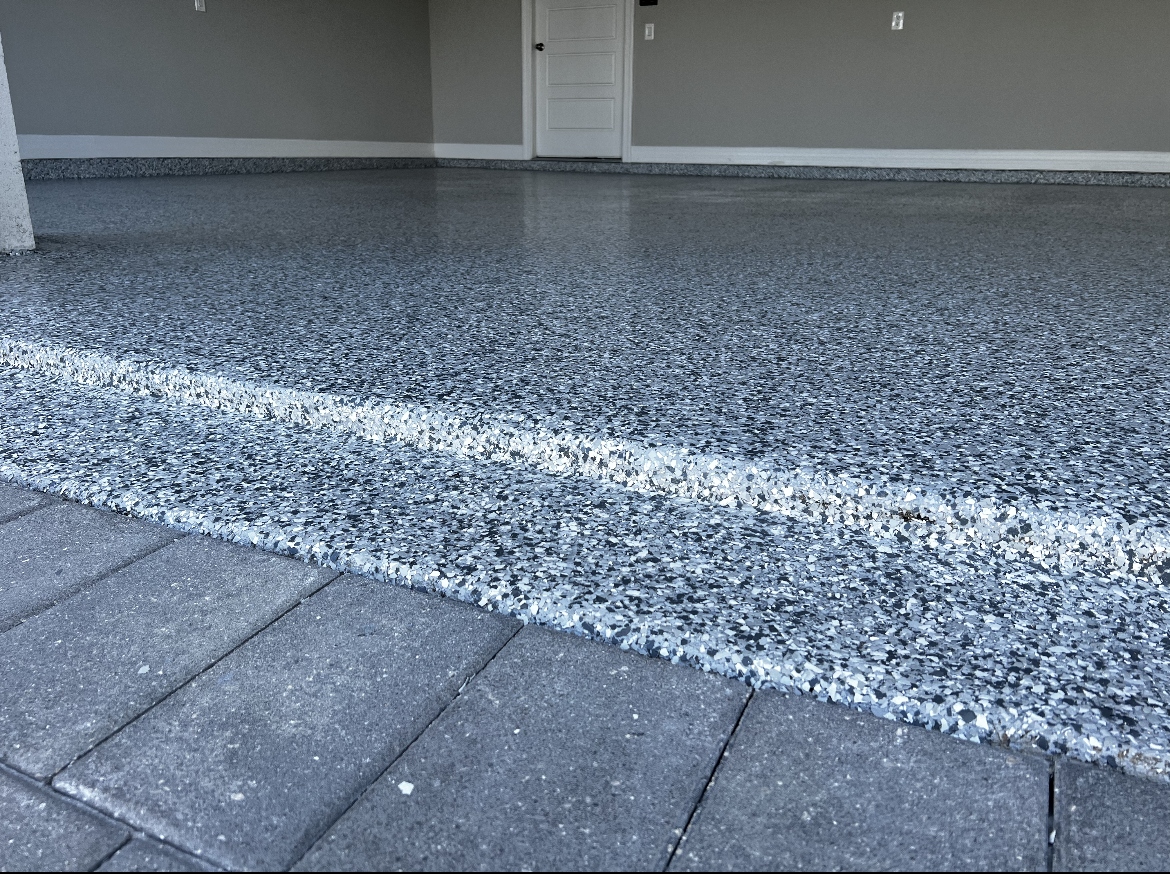 Low-angle view of a gray pebble-finish patio step beside dark stone pavers and a closed garage door