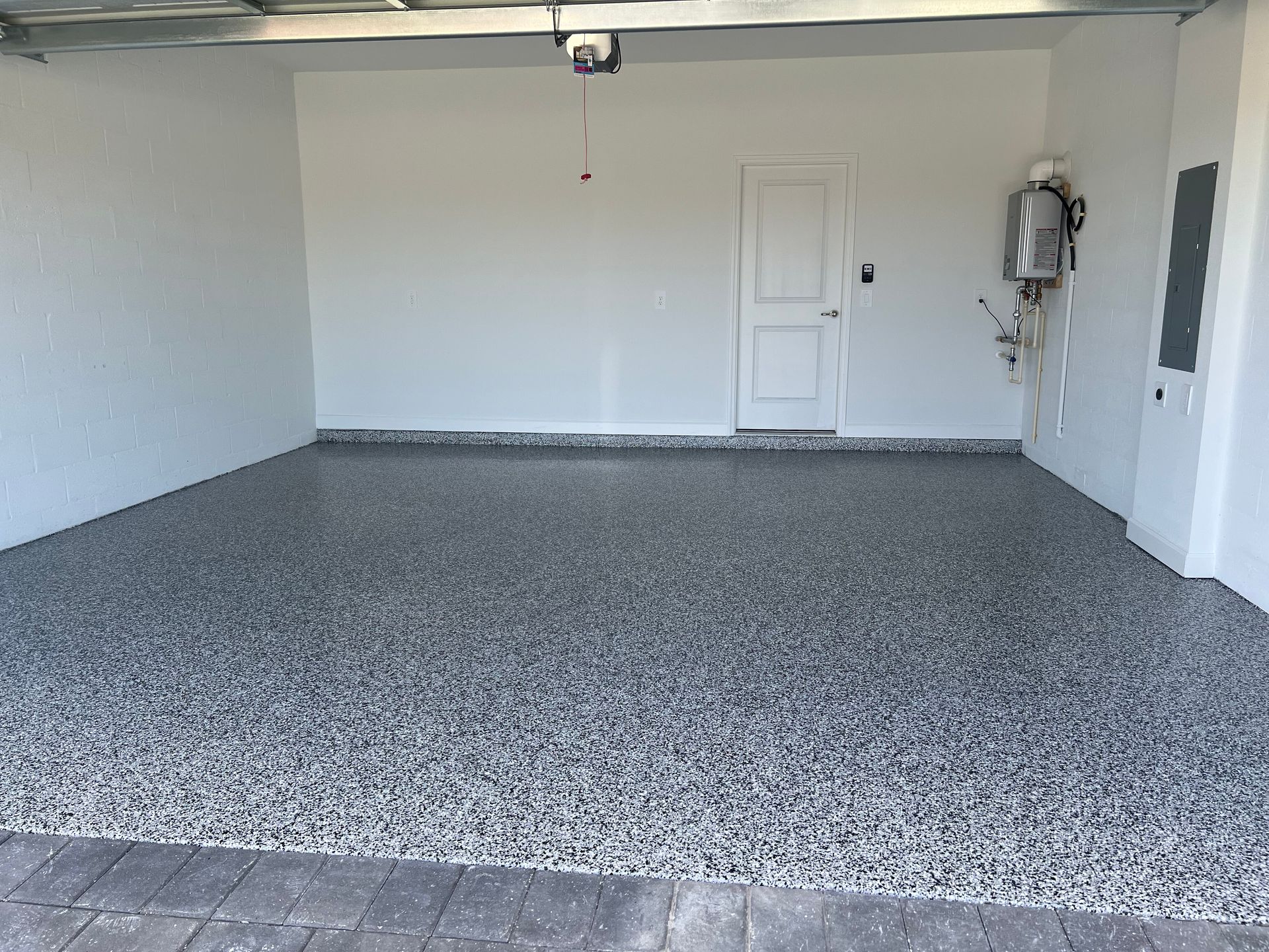 Empty garage with speckled gray floor, white walls, a side door, and a water heater on the right.