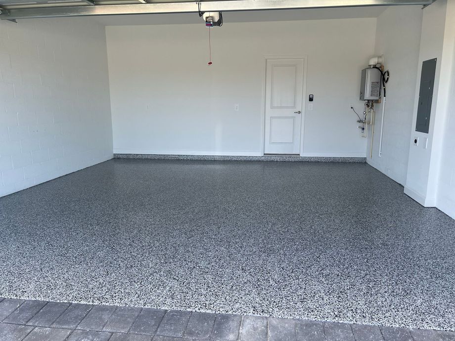 Empty gray garage with speckled floor, white walls, closed door, and utility equipment on the right.