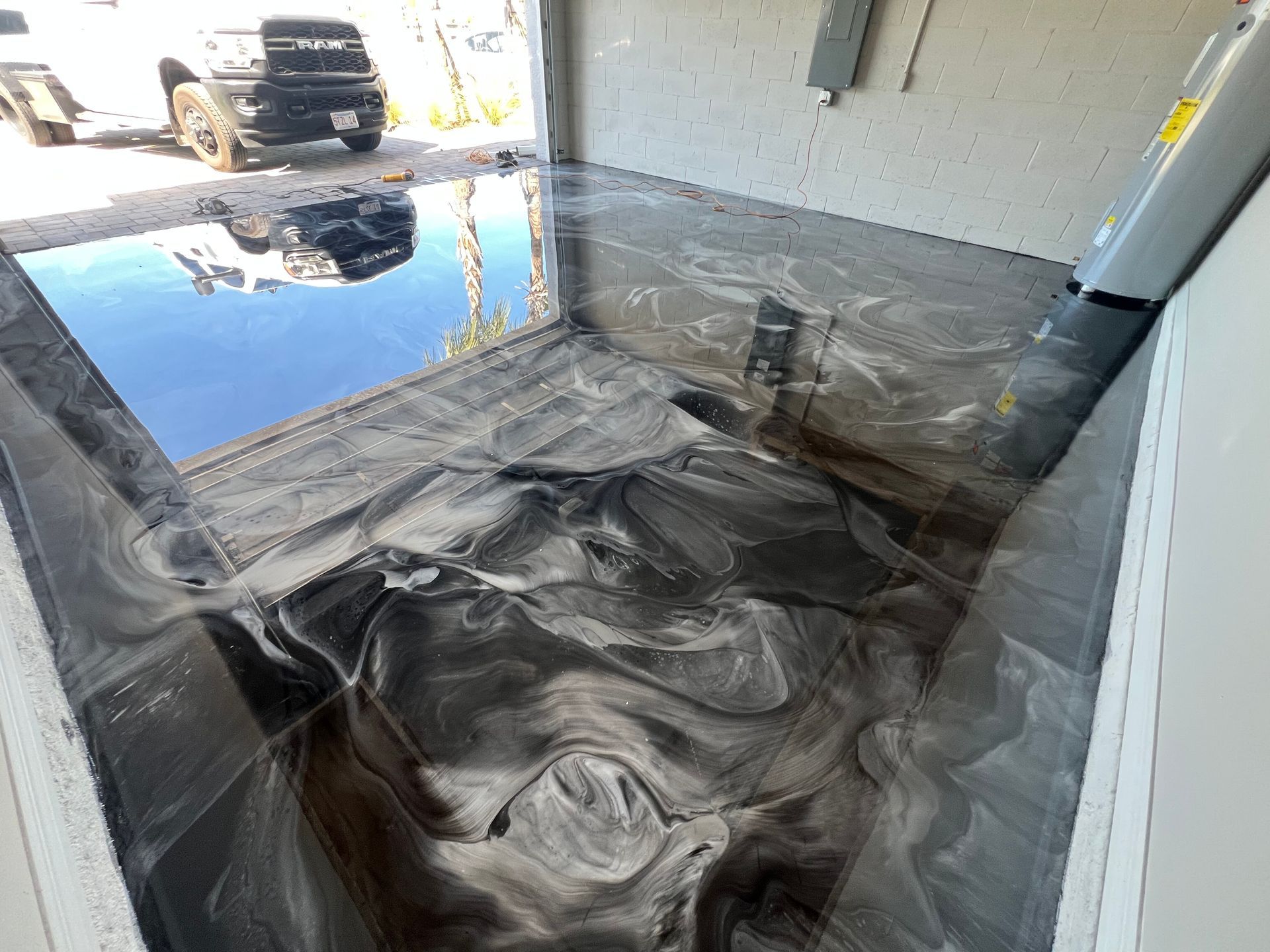 Flooded garage floor reflecting a blue truck outside, with water pooling over the concrete.
