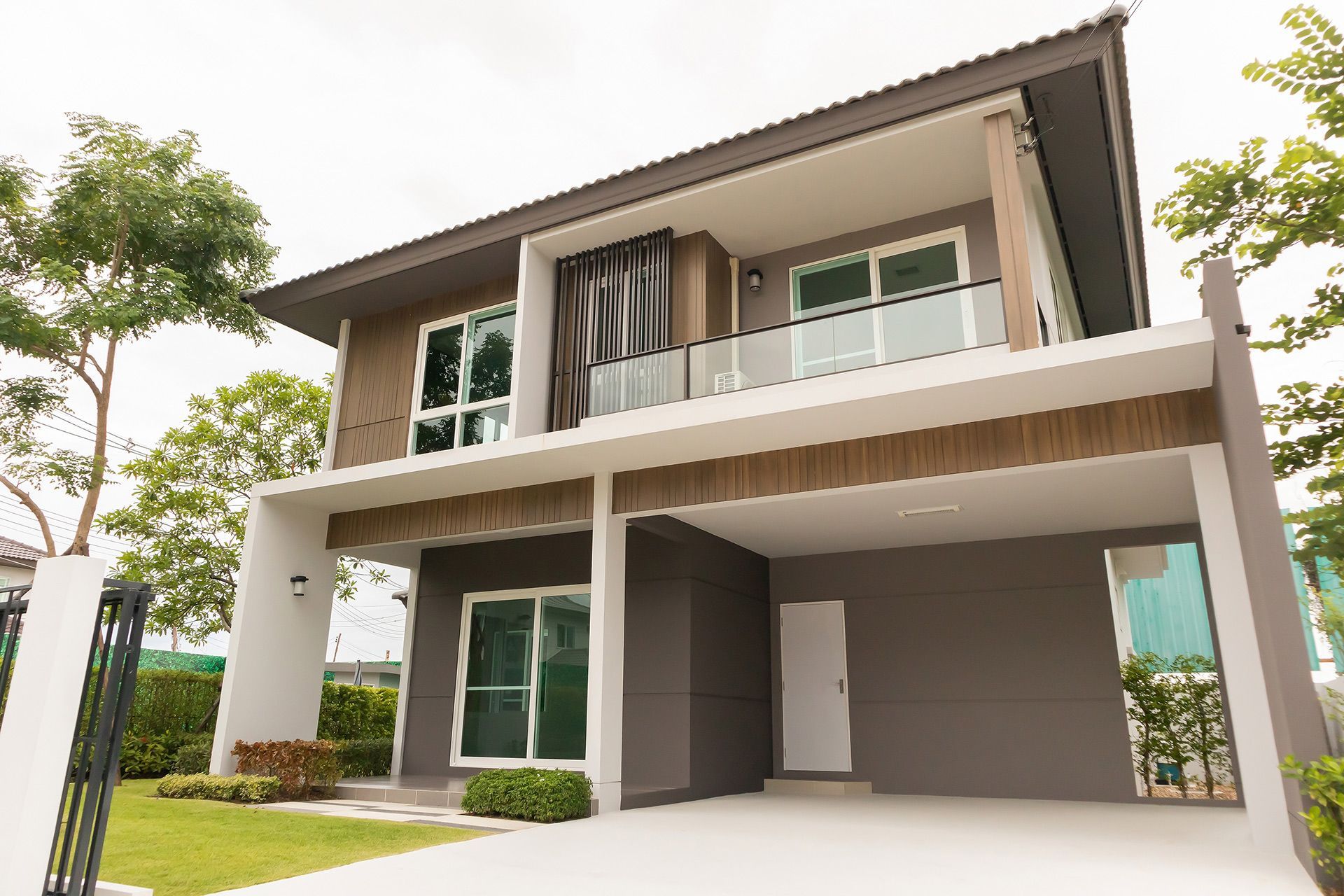 Modern two-story house with gray and white exterior, featuring a carport and glass balconies.