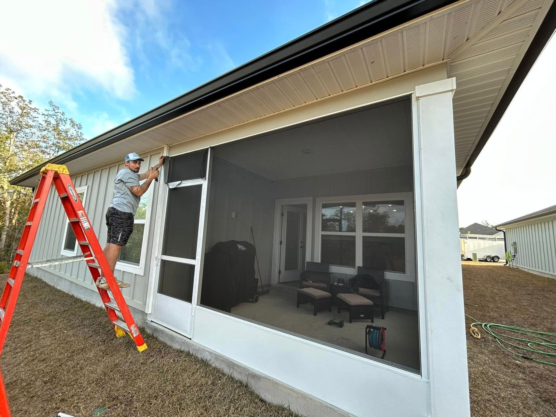 A man is standing on a ladder in front of a screened in porch. A man is standing on a ladder in front of a screened in porch.