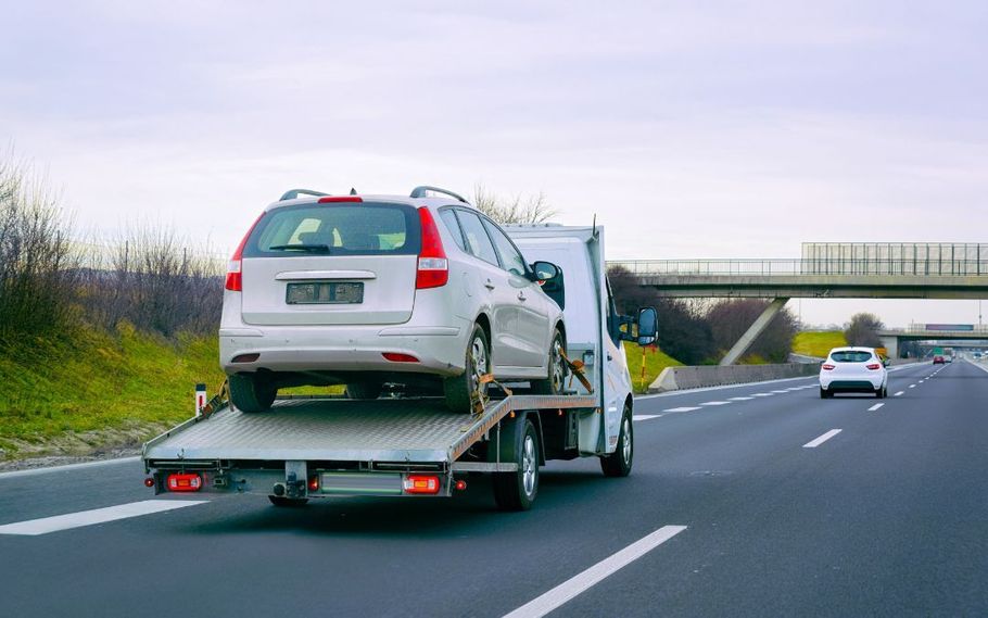 Car carrier truck hauling a silver SUV on a highway near an overpass