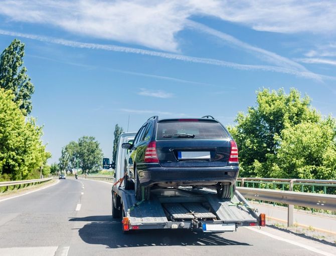 Black SUV loaded on a car trailer driving on a sunny highway