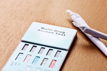 Medical professional drawing blood from a patient's finger for a COVID-19 test; test materials on white table.