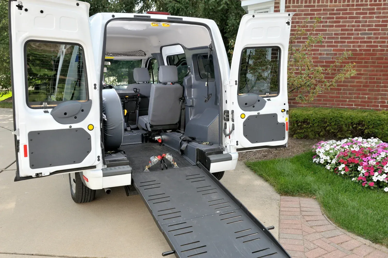 White van with rear doors open, ramp extended, parked on a driveway.