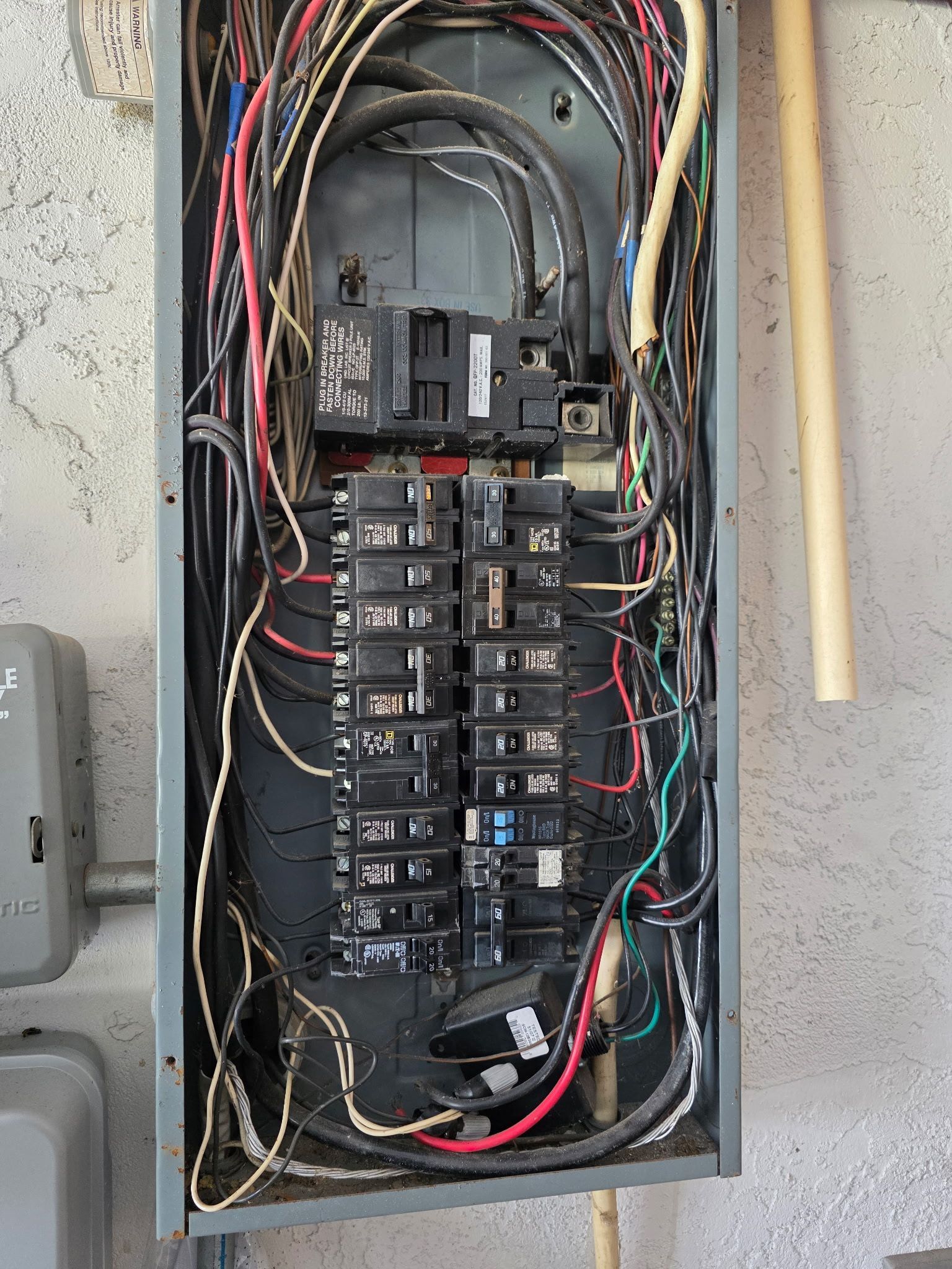 Open electrical breaker panel with tangled red, black, and white wiring in a wall cavity.