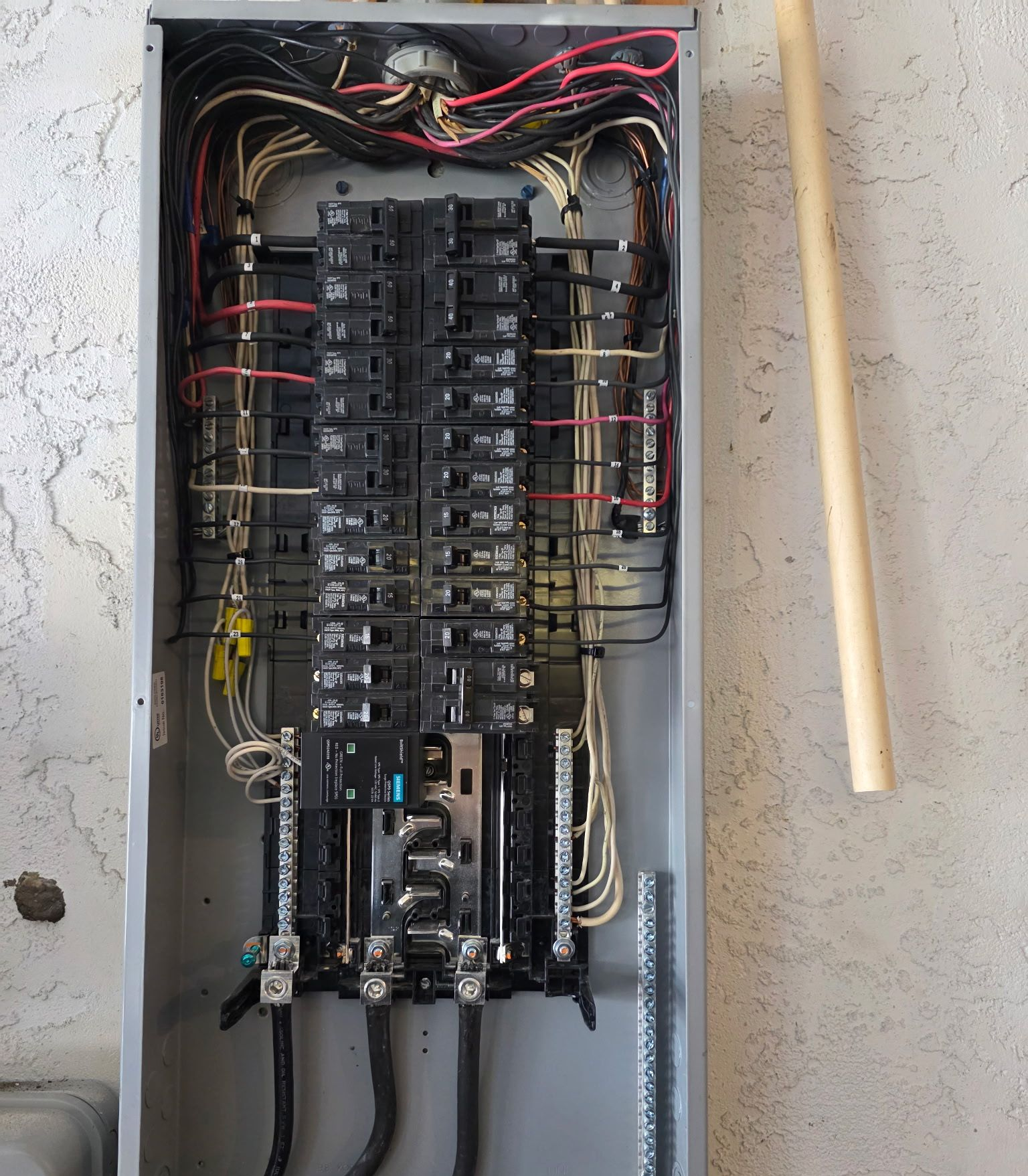 Open electrical breaker panel with many wires and switches mounted on a wall.