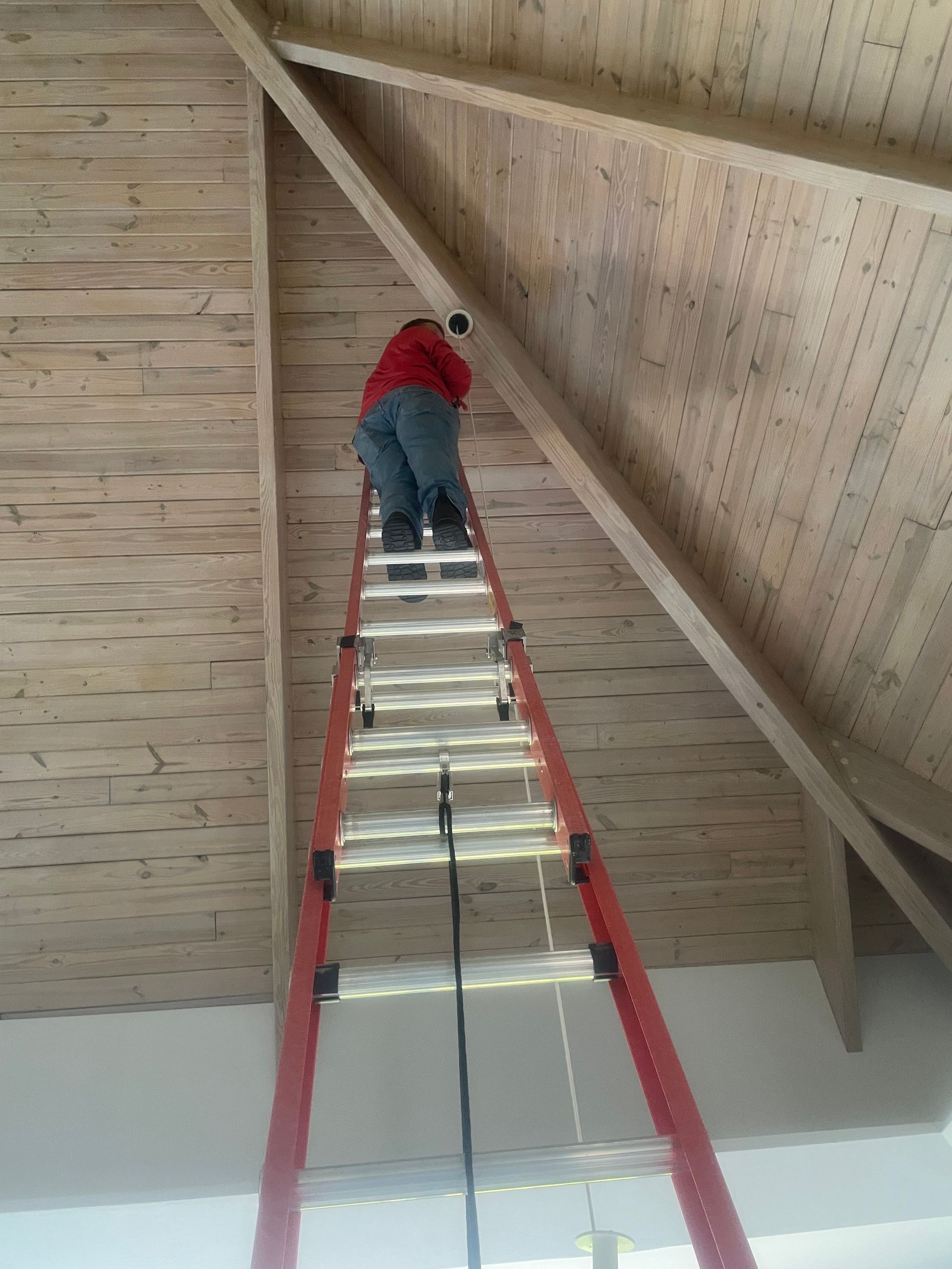 Person on a red ladder working on a high wooden ceiling.
