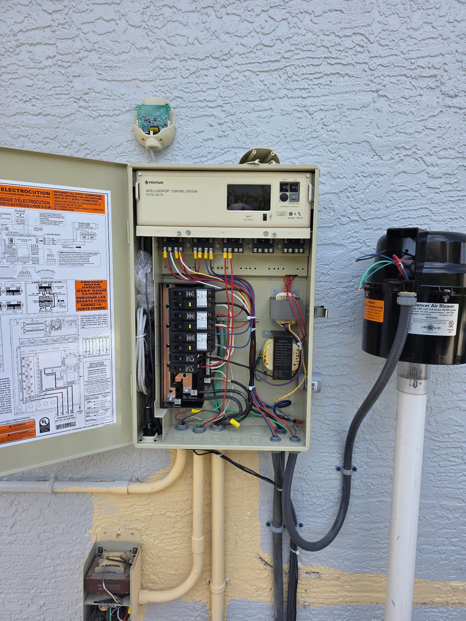 Open electrical control panel mounted on a stucco wall beside a meter box and utility conduits.