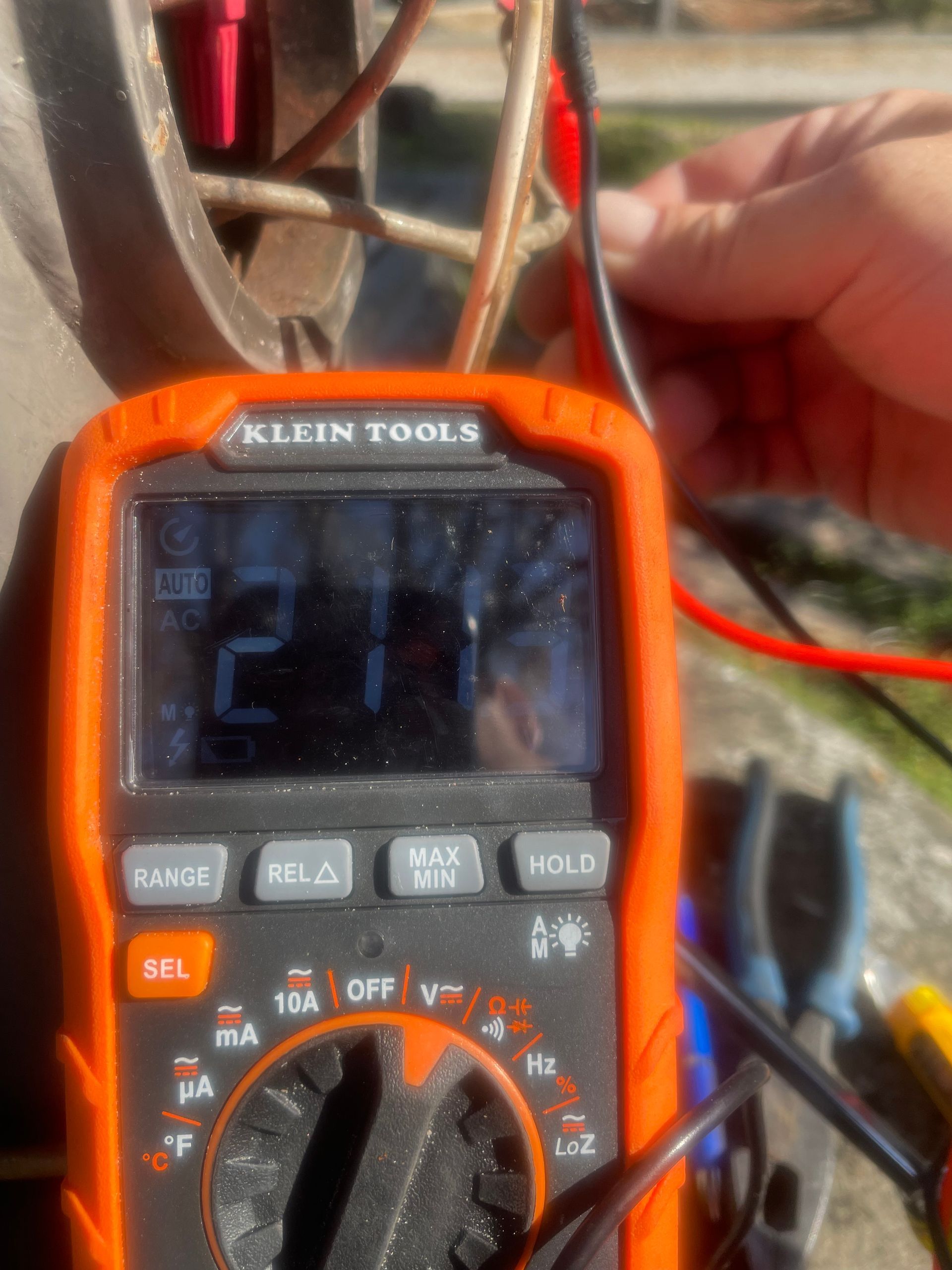 Hand holding a Klein Tools digital multimeter with red and black test leads attached.