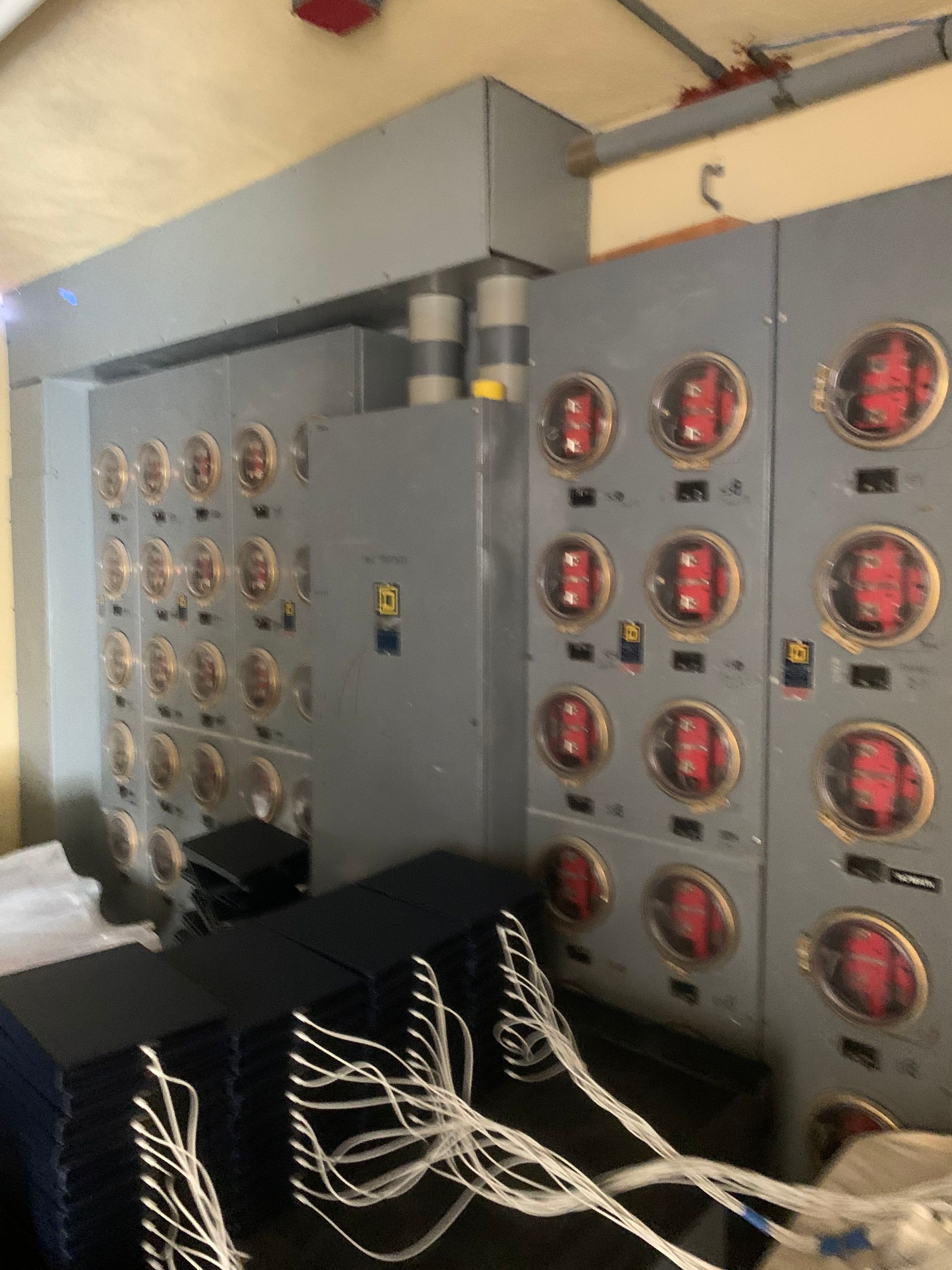 Electrical control panels with many red gauges and loose white cables in an industrial room