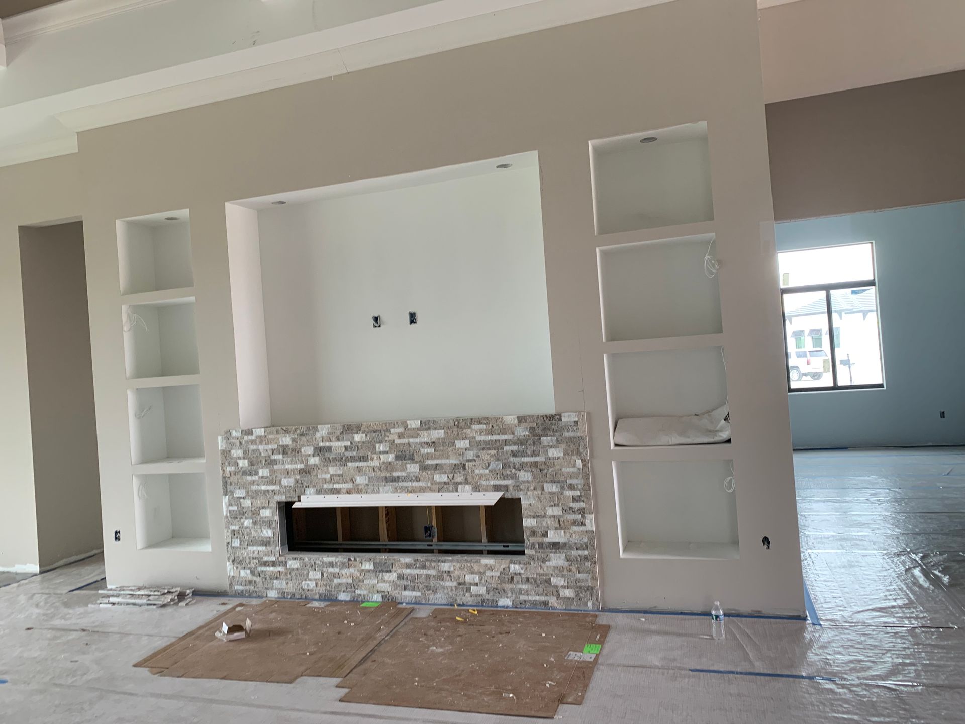 Living room with a gray tile fireplace surround, built-in shelves, and unfinished flooring.