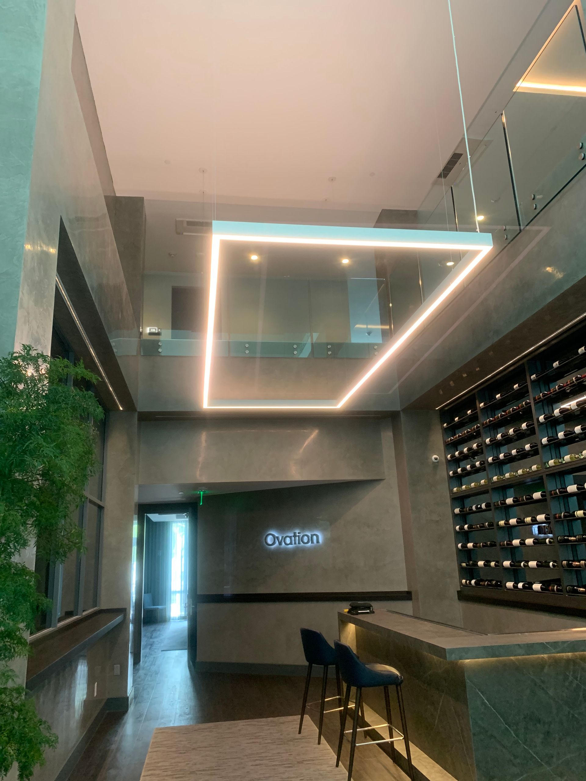 Modern bar interior with geometric ceiling lights, wine wall, and high stools