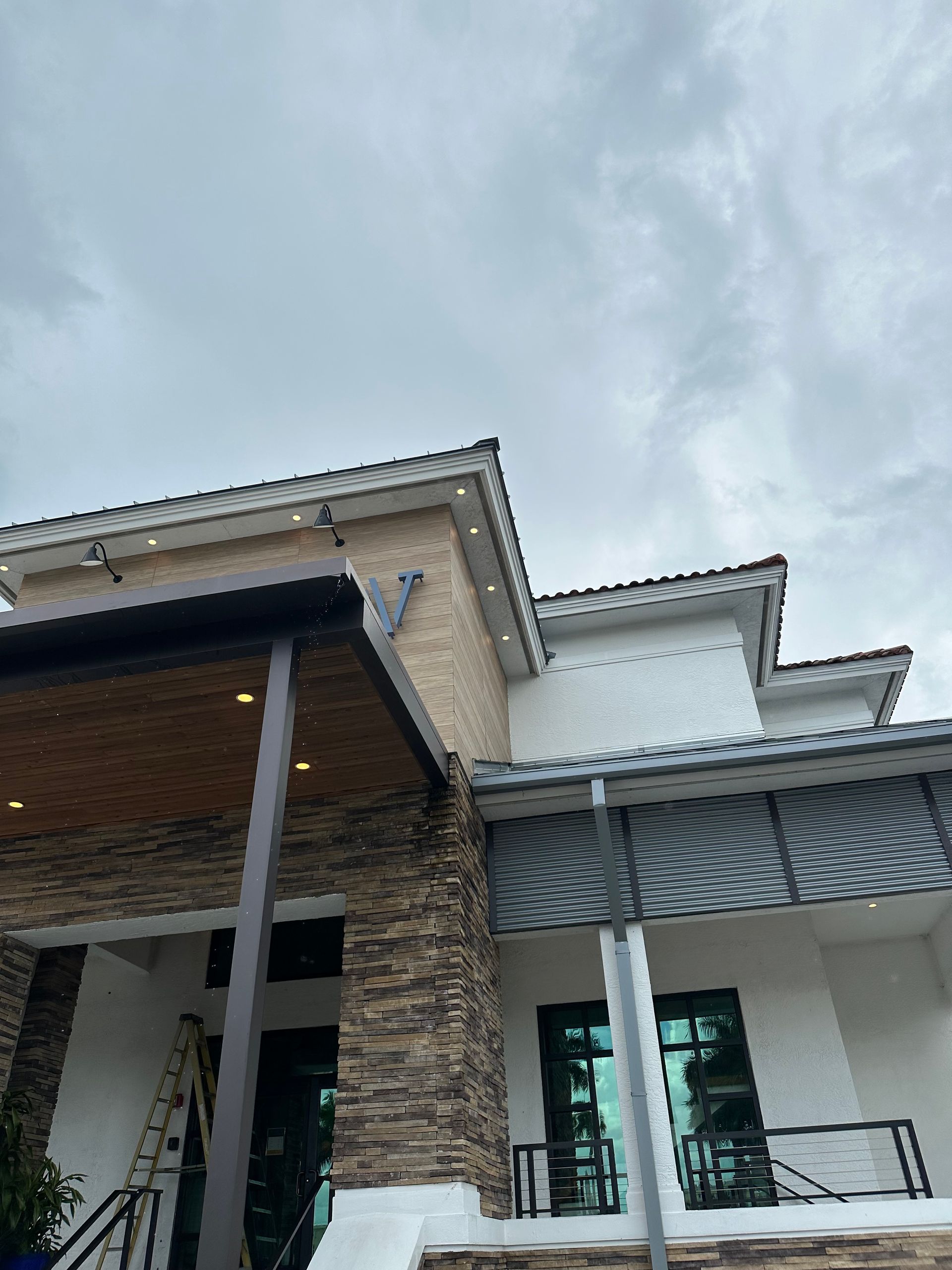 Low-angle view of a house exterior with tiled roof, stone columns, and a cloudy sky