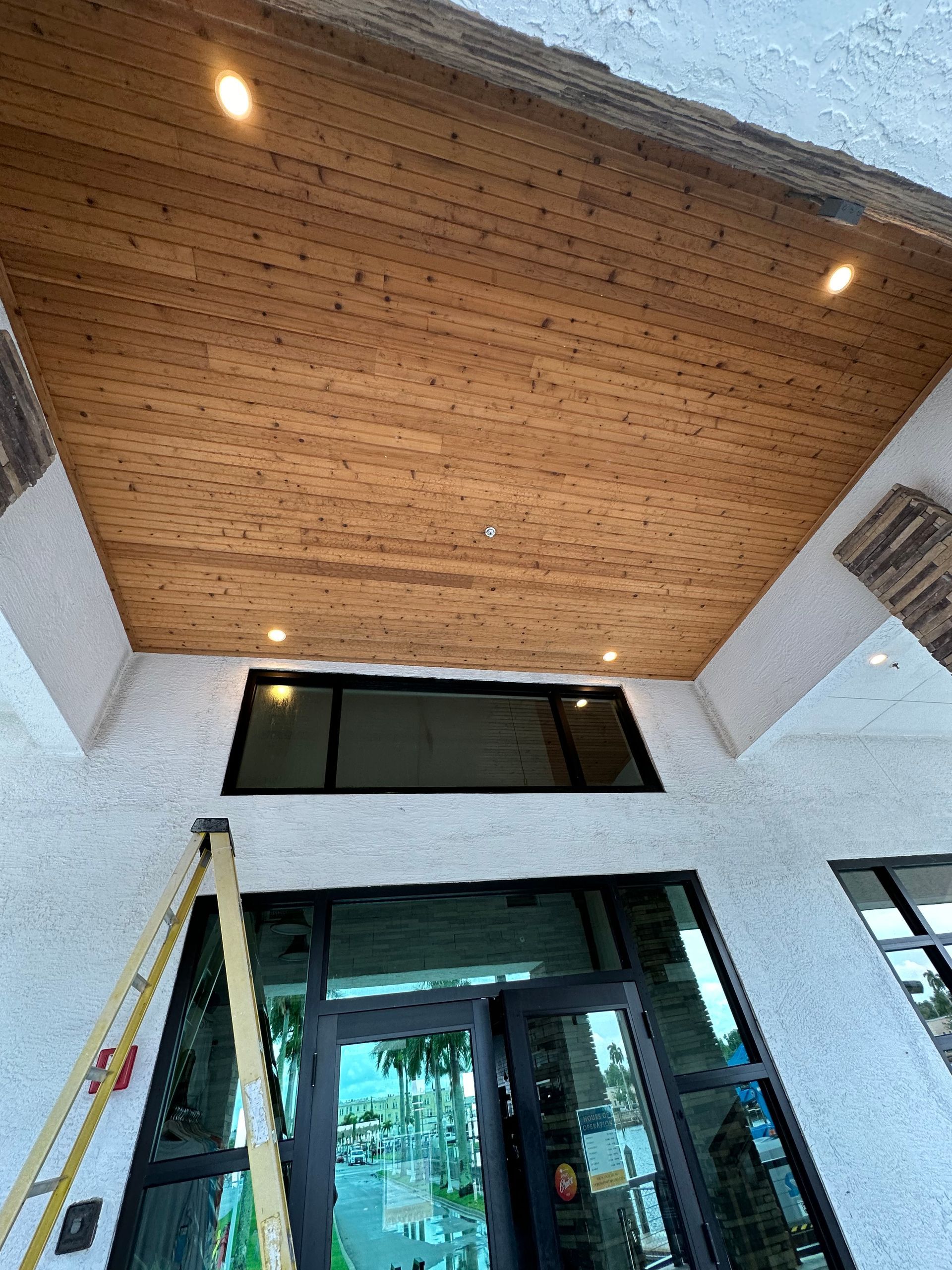 Entrance with glass doors, white walls, and a wood-paneled ceiling, viewed from below.